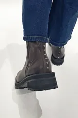 Bota de cuero color chocolate, con caña media, cierre lateral y tachas decorativas en la parte trasera.