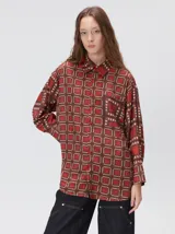 Camisa de seda con estampado geométrico de cuadrados en tonos rojizos y marrones. Presenta cuello camisero, cierre frontal con botones, bolsillo en el pecho y mangas largas con puños abotonados.