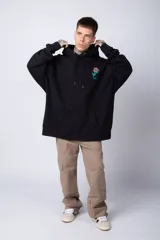 Buzo tipo canguro de corte oversize, color blanco, con capucha y cordones ajustables. Presenta un pequeño estampado de una rosa roja en el pecho y un bolsillo frontal tipo canguro.