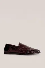 Mocasín de cuero marrón con textura croco y acabado brillante, de diseño clásico con detalle de antifaz en el empeine y costuras pespunteadas alrededor de la puntera.