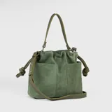 Cartera tipo bucket de cuero gamuzado color verde oliva, con correa de hombro y correa bandolera ajustable. Tiene dos bolsillos externos, cierre con broche imán y forro interno de gabardina de algodón con tres compartimentos.