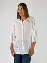 Camisa blanca con cuello camisero, cierre frontal de botones y mangas tres cuartos abullonadas con bordados suizos y detalles perforados en los laterales y mangas.