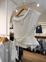 Blusa blanca de diseño asimétrico con cuello cruzado, manga corta y detalle de lazo lateral en la cintura.