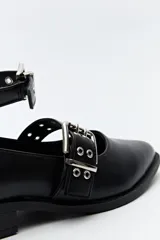 Zueco de diseño contemporáneo con inspiración punk, confeccionado en material símil cuero, con doble tira con hebillas metálicas y tachas, y taco bajo.