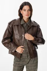Chaqueta de cuero sintético en color chocolate, con diseño de hombreras marcadas, cuello clásico y cierre frontal con botones metálicos a presión. Presenta un acabado texturizado y bolsillos frontales integrados.