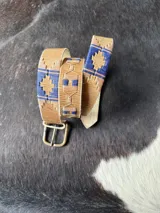 Cinto de cuero marrón claro con detalles bordados geométricos en tonos azul, rojo y beige, hebilla metálica de bronce y puntera forrada en cuero.