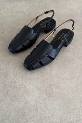 Sandalias de cuero color negro, estilo romanas con tiras entrelazadas en la parte delantera, talón descubierto y tira ajustable con hebilla metálica.