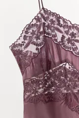 Vestido midi satinado de corte lencero, con escote en pico y tirantes finos. Presenta detalles de bordados florales y aplicaciones de encaje en la parte superior.