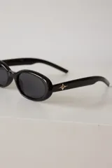 Lentes de sol con armazón ovalado de color negro y cristales tonalidad marrón. Presentan un detalle metálico en forma de estrella en las patillas.