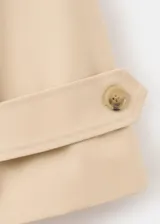 Chaqueta corta de algodón color beige, de corte holgado, con cuello clásico, cierre frontal de botones y bolsillos ribeteados. Cuenta con mangas largas amplias con puños ajustables mediante tiras y botones.