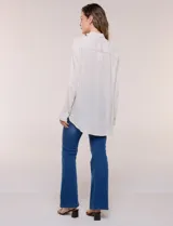 Camisa Magaschoni de silueta holgada y tejido texturizado color blanco, con cuello camisero, cierre frontal de botones, mangas largas con presilla para arremangar y diseño asimétrico con espalda más larga.