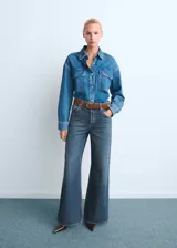 Pantalón de jean estilo wide leg con tiro alto, confeccionado en tejido de algodón. Presenta diseño de cinco bolsillos, cierre de botones y trabillas para cinturón.