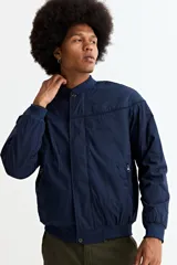Campera tipo bomber color tostado, con cierre frontal, cuello, puños y ruedo de tejido elástico acanalado. Presenta costuras horizontales en la parte superior del pecho.