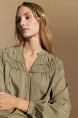 Camisa de manga larga color blanco, con cuello mao y escote en V. Presenta frunces en el canesú, cierre frontal con botones y mangas amplias con puños abotonados.