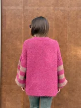 Buzo de tejido de punto con textura peluda, de corte holgado y mangas amplias. Presenta un diseño geométrico con una flor grande estampada en el centro, combinando tonos fucsia, rosa y marrón en un patrón de bloques y rayas.