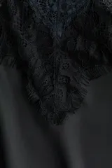 Vestido corto lencero de satén negro, con escote en V pronunciado y ribetes de encaje floral en el escote y el bajo. Cuenta con finos tirantes spaghetti cruzados en la espalda.
