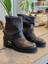 Botas de cuero negro con efecto desgastado en tono marrón, diseño de caña media, punta redondeada, taco bajo y detalle de hebilla metálica lateral.