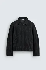 Cazadora de corte regular fit confeccionada en tejido jacquard con textura abstracta. Presenta cuello solapa, cierre frontal de cremallera, bolsillos de vivo en la cadera y mangas largas con puños ajustables mediante botón a presión oculto.