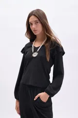 Blusa negra de manga larga con textura, cuello en V y detalle de volados en los hombros. Presenta mangas con puños elásticos y un corte recto.