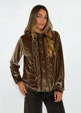 Camisa de terciopelo color bordó, con cuello mao y cierre frontal de botones. Presenta detalles de volados verticales a ambos lados de la botonera y mangas largas con puños abotonados.