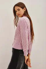 Cardigan de punto calado en color rosado, con cuello redondo y cierre frontal de botones decorativos con pedrería brillante.