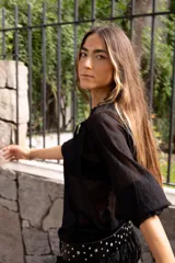 Blusa de plumeti color bordó, con cuello alto ajustable mediante lazo, mangas largas con puños elásticos y detalle de volados en las terminaciones.