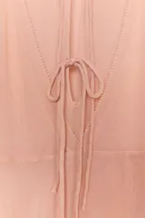Blusa de viscosa color rosado con cuello redondo, manga larga abullonada con puños elásticos y cierre frontal con lazadas. Presenta un diseño con volantes en el bajo y corte asimétrico.