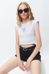 Top corto de tejido de punto acanalado color lila claro, con hombreras marcadas y un pequeño bordado de corazón en llamas en el centro del pecho.