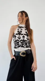 Top de seda color crema con estampado de flores negras, cuello halter y lazo en la espalda.