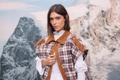 Chaleco acolchado con diseño a cuadros en tonos marrones y blancos, con cuello y solapa frontal en pana marrón. Presenta cierre con botones metálicos y detalles de costura en los hombros.