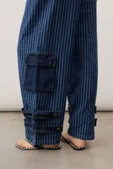 Jean de corte cargo y estilo holgado, con diseño de rayas verticales en tonos de azul. Presenta bolsillos laterales con solapa y detalles de tiras ajustables con hebillas en los tobillos.