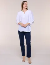 Blusa blanca de rayón y poliéster con textura, escote en V y delicados bordados al tono sobre el canesú. Cuenta con mangas raglán tres cuartos abullonadas con puños elastizados y diseño holgado.