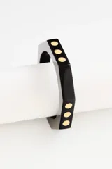 Pulsera rígida de resina negra con diseño octogonal y detalles de puntos metálicos dorados incrustados.
