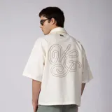 Camisa de manga corta color marfil, confeccionada en 100% algodón con calce boxy, cuello camisero, cierre frontal de botones y diseño con bordado sutil en la parte inferior.