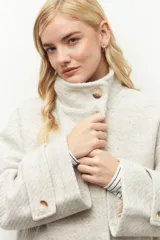 Tapado corto color crema de cuello alto con grandes botones veteados y dos bolsillos delanteros.