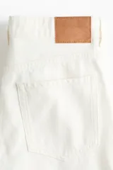 Jean de corte wide leg en denim de algodón rígido, con diseño de cinco bolsillos, cintura clásica con cierre de botones y piernas amplias.