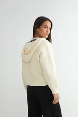 Abrigo negro con capucha, confeccionado en tejido de textura suave. Presenta cierre frontal con cremallera, bolsillos laterales integrados con costuras decorativas y puños ajustados.
