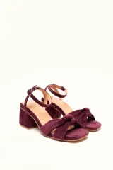 Sandalia de tacón cuadrado medio, confeccionada en terciopelo color bordó. Presenta una tira frontal con detalle de nudo y una pulsera ajustable al tobillo con hebilla metálica.