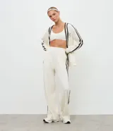Pantalón deportivo de corte oversized estilo college, confeccionado en microfibra color crema con rayas laterales contrastantes en color marrón. Presenta cintura fija, bolsillos funcionales y frisos frontales.