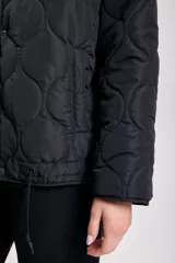 Campera capitoneada negra con diseño acolchado, cierre frontal con botones a presión, capucha con cordón ajustable y cordón en el ruedo.
