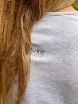 Remera de manga larga color gris melange, con cuello redondo y detalle de texto bordado en el pecho.