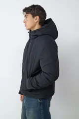 Campera acolchada negra con capucha integrada, cierre frontal de cremallera y bolsillos laterales con cierre.