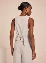 Chaleco sastrero color gris claro con patrón de cuadros, escote en V, cierre frontal con botones y bolsillos delanteros decorativos.