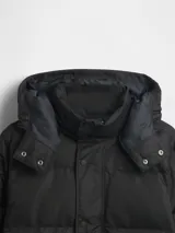 Campera puffer negra con capucha desmontable, cierre frontal con botones a presión y bolsillos laterales. Cuenta con puños internos acanalados para mayor protección contra el frío.