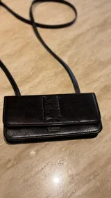Cartera tipo bandolera de cuero negro, con diseño rectangular y solapa frontal con detalle de trenzado vertical. Incluye correa larga regulable y cierre con botón imantado.
