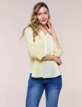 Blusa estampada en tonos amarillo y blanco, con escote en V, cuello solapa y media abotonadura frontal con botones nacarados. Presenta finas alforzas verticales en la pechera y mangas tres cuartos con puños elastizados en punto smock. Confeccionada en rayón y poliéster.