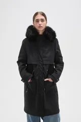 Campera parka negra de corte largo y holgado, con capucha fija adornada con piel sintética, cierre frontal oculto y bolsillos laterales con cordones ajustables en la cintura.