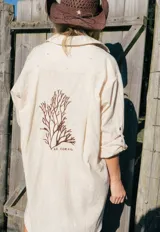 Túnica camisera de lino color beige, de corte largo y holgado, con mangas largas y bordado en la espalda con motivo de coral y texto.