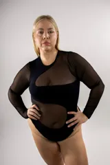 Body de algodón elastizado color negro con diseño asimétrico de ondas y detalles combinados en microtul transparente, de manga larga y cuello redondo.
