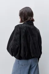 Campera marrón de poliuretano con acabado texturizado, silueta relajada, cuello camisero, cierre frontal, hombros caídos y mangas amplias con efecto abombado.